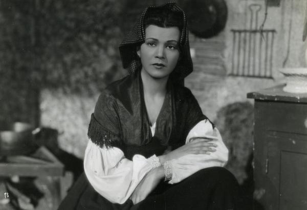 Scena del film "Gelosia" - Poggioli, Ferdinando Maria, 1943 - Mezza figura di Luisa Ferida seduta con le braccia conserte mentre guarda davanti a lei.