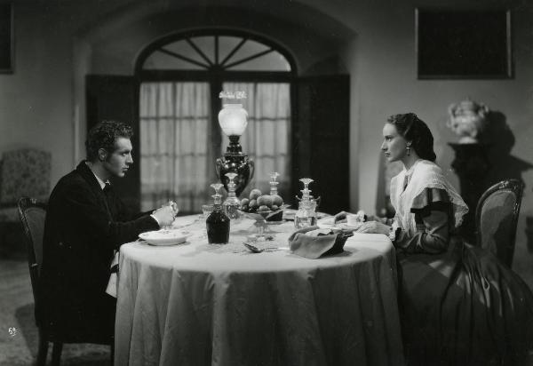 Scena del film "Gelosia" - Poggioli, Ferdinando Maria, 1943 - Seduti uno di fronte all'altro a una tavola imbandita: Elena Zareschi e Roldano Lupi si guardano intensamente. Lui sta sbucciando una mela.