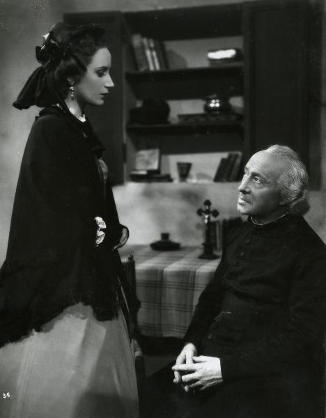 Scena del film "Gelosia" - Poggioli, Ferdinando Maria, 1943 - A sinistra in piedi, Elena Zareschi, con le braccia conserte, guarda Ruggero Ruggeri seduto di fronte a lei. L'attore ricambia lo sguardo.