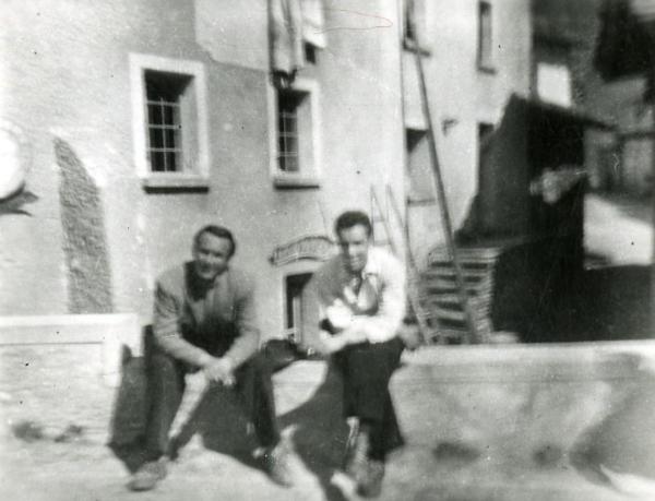 Fotografia sul set "Gente così" - Cerchio, Fernando, 1949 - Seduti su un muretto: a sinistra, l'attore Adriano Rimoldi, a destra, il regista Fernando Cerchio mentre guardano verso la cinepresa.