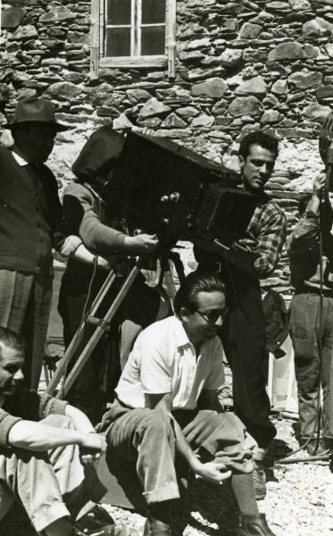 Fotografia sul set "Gente così" - Cerchio, Fernando, 1949 - Mentre si sistema un calzino, il regista Cerchio. Dietro, con un cappello, il direttore della fotografia Arturo Gallea. Insieme a loro, un gruppo di operatori non identificati.