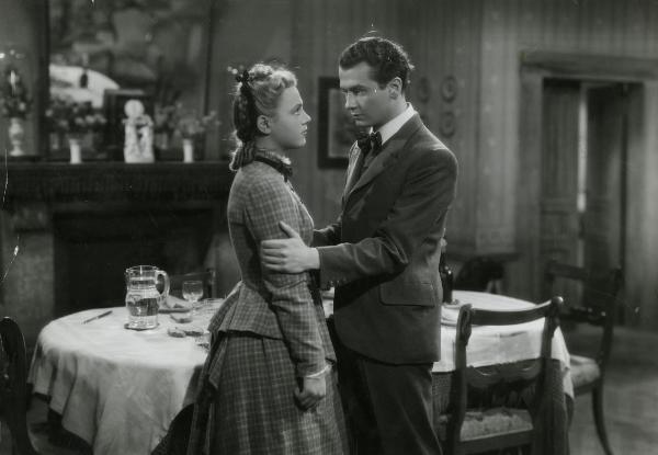 Scena del film "La Gerla di papà Martin" - Bonnard, Mario, 1940 - In una sala da pranzo: Roberto Villa tiene per le braccia Luisella Beghi. Entrambi si guardano negli occhi.