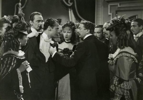 Scena del film "La Gerla di papà Martin" - Bonnard, Mario, 1940 - Cesare Fantoni, a destra, e Roberto Villa, a sinistra, si tengono per il bavero della giacca. In mezzo, Maria Mercander. Dietro, Roberto Villa e Nino Crisman.