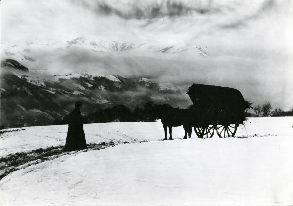 Scena del film "Giacomo l'idealista" - Lattuada, Alberto, 1942 - In un paesaggio montano innevato: un'attrice non identificata cammina verso una carrozza con dei cavalli trainata da un altro attore non identificato.