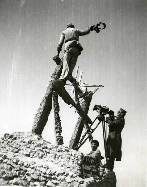 Fotografia sul set di "Giarabub" - Alessandrini, Goffredo, 1942 - Su un trabicolo di legno e pietra, tre operatori non identificati sono alle prese con le riprese del film.