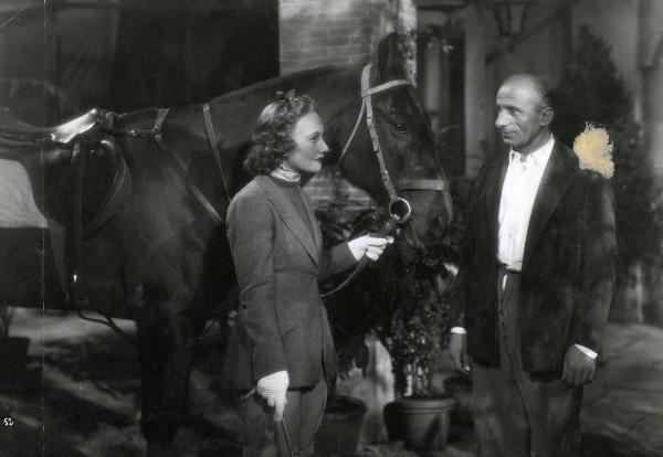 Scena del film "Gioco pericoloso" - Malasomma, Nunzio, 1942 - A sinistra, Elsa Merlini, in tenuta da cavallerizza, tiene un cavallo per le briglie. A destra, Fausto Guerzoni la guarda.