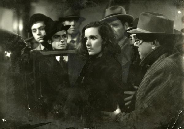 Scena del film "Gioco pericoloso" - Malasomma, Nunzio, 1942 - Al centro, Elisa Cegani, guardando dritto davanti a sé, sta per entrare in un automobile. Attorno, attori non identificati la guardano.