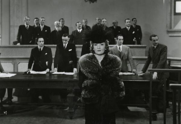 Scena del film "Gioco pericoloso" - Malasomma, Nunzio, 1942 - In un'aula di tribunale: in primo piano Elsa Merlini guarda dritto davanti a sé. Dietro, alcuni attori non identificati.