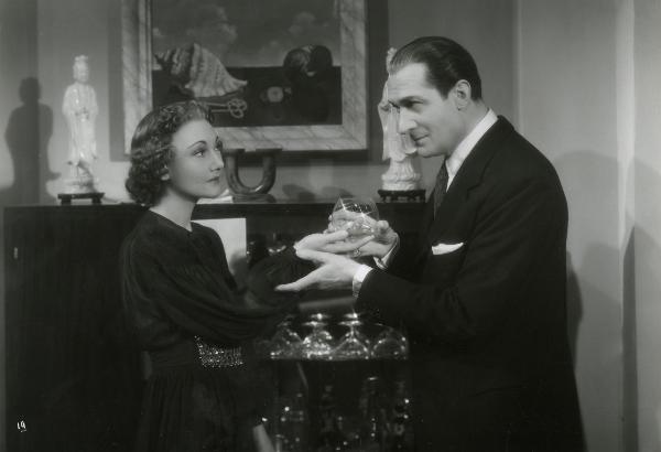 Scena del film "Gioco pericoloso" - Malasomma, Nunzio, 1942 - In una sala: a sinistra, Elsa Merlini porge un bicchiere da brandy a Nerio Bernardi. L'attore, a destra, accoglie il bicchiere con un gesto delle mani.