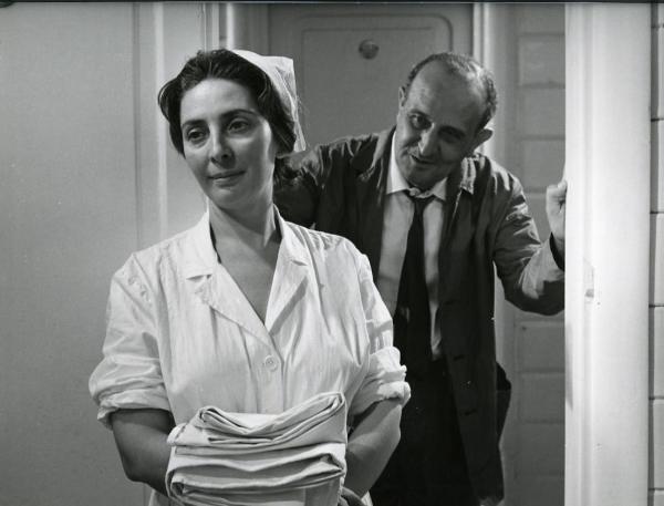 Scena del film "I giorni contati" - Petri, Elio, 1962 - In primo piano, Regina Bianchi, in veste da infermiera, tiene dei panni tra le mani. Dietro di lei, Salvo Randone che, appoggiato con le mani agli stipiti della porta, la guarda.