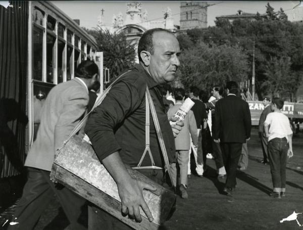 Scena del film "I giorni contati" - Petri, Elio, 1962 - Mezza figura di Salvo Randone fuori da un tram. L'attore tiene sulla spalla, grazie a una tracolla, una cassetta metallica mentre con la mano sinistra tiene un giornale.