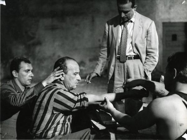 Scena del film "I giorni contati" - Petri, Elio, 1962 - Al centro, Salvo Randone con il braccio destro appoggiato a dei mattoni. Paolo Ferrari, dietro, gli tiene la testa. Un attore non identificato sembra fargli una puntura.