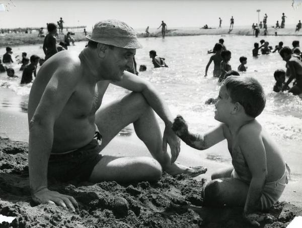 Scena del film "I giorni contati" - Petri, Elio, 1962 - Sul bagnasciuga: Salvo Randone, a sinistra, sorride a un bambino non identificato che gioca, a destra. In mare, molti attori non identificati.