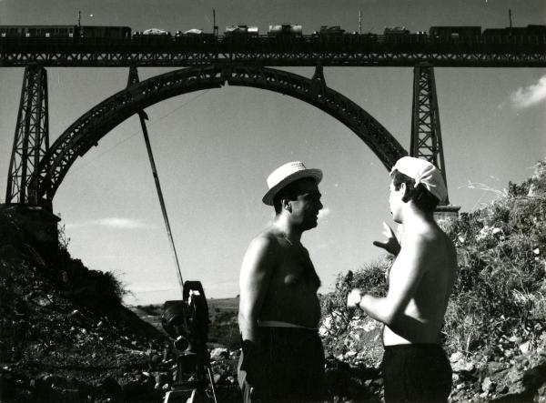 Fotografia sul set di "Un giorno da leoni" - Loy, Nanni, 1961 - A sinistra, Marcello Gatti con cappello di paglia, a destra, un operatore non identificato. Entrambi sono vicini al ponte in miniatura da far saltare.