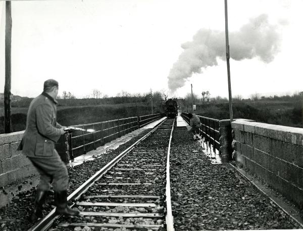 Scena del film "Un giorno da leoni" - Loy, Nanni, 1961 - A sinistra, un attore non identificato su dei binari, spara al treno in corsa. A destra, un altro attore non identificato tira delle leve.