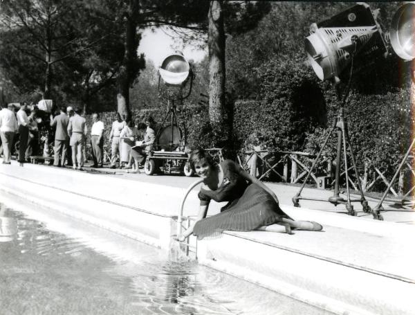 Fotografia sul set di "Giovani mariti" - Bolognini, Mauro, 1957 - L'attrice Antonella Lualdi a bordo piscina mentre tocca l'acqua. Attorno, la troupe e le macchine per la ripresa.