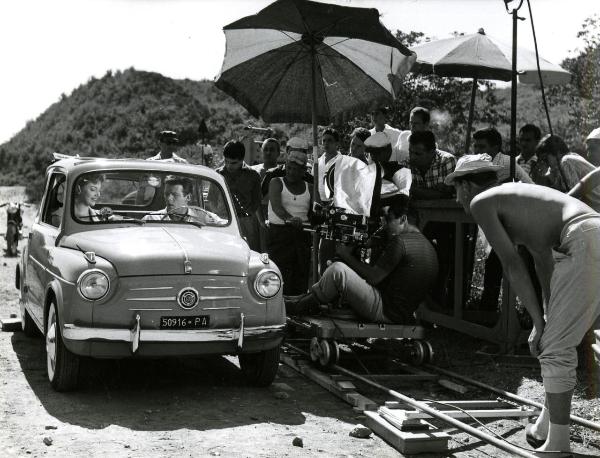 Fotografia sul set di "Giovani mariti" - Bolognini, Mauro, 1957 - A sinistra, in un'automobile, due attori non identificati. A destra, alla camera, Marcello Gatti. Alle sue spalle, la troupe.