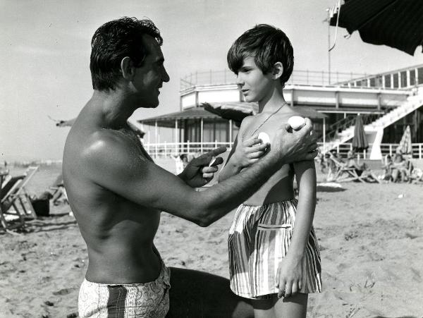 Scena del film "Il giovedì" - Risi, Dino, 1964 - Su una spiaggia, Walter Chiari è in ginocchio davanti a Roberto Ciccolini. I due tengono in mano delle conchiglie e si guardano l'un l'altro.