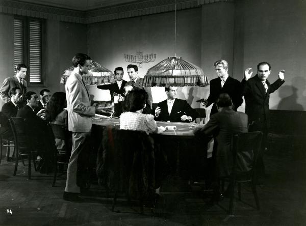 Scena del film "Gioventù perduta" - Germi, Pietro, 1947 - Seduti a un tavolo da poker, molti attori non identificati. A destra, con in mano una pistola, Jacques Sernas.