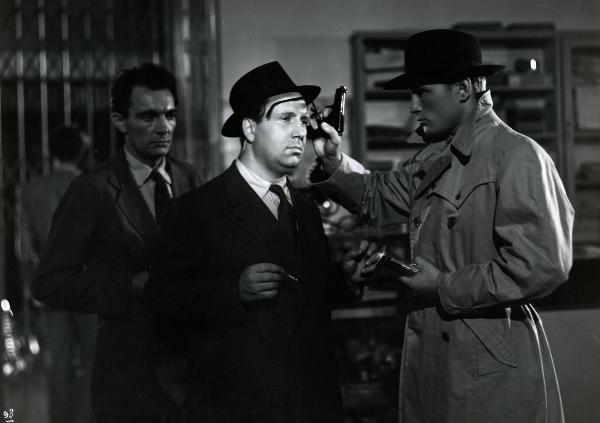 Scena del film "Gioventù perduta" - Germi, Pietro, 1947 - A destra, Jacques Sernas, tenendo la pistola con una mano, con la stessa toglie gli occhiali a un attore non identificato, in centro. Dietro, un attore non identificato.