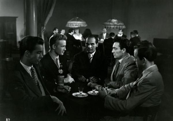Scena del film "Gioventù perduta" - Germi, Pietro, 1947 - Attorno a un tavolino: in primo piano due attori non identificati. In secondo piano, Jacques Sernas, a sinistra, e Massimo Girotti a destra. In mezzo a loro, un altro attore non identificato.