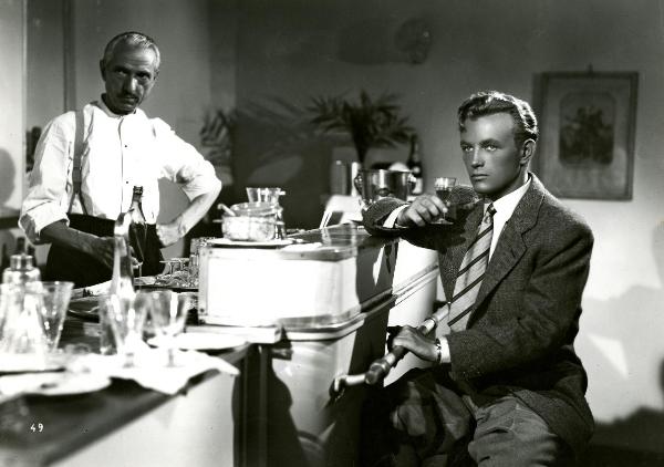 Scena del film "Gioventù perduta" - Germi, Pietro, 1947 - Appoggiato al bancone di un bar, Jacques Sernas, tenendo nella mano destra un bicchiere, guarda dritto davanti a sé. Dietro il bancone, un attore non identificato.
