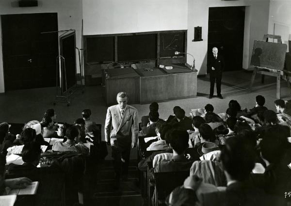 Scena del film "Gioventù perduta" - Germi, Pietro, 1947 - In un'aula universitaria, molti attori non identificati in veste di studenti fanno lezione. Al centro, Jacques Sernas sta salendo le scale dell'aula.