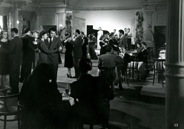 Scena del film "Gioventù perduta" - Germi, Pietro, 1947 - In una sala da ballo, molti attori non identificati danzano e si ristorano stando seduti. A sinistra, Carla Del Poggio, con un vestito a pois, e Massimo Girotti ballano.