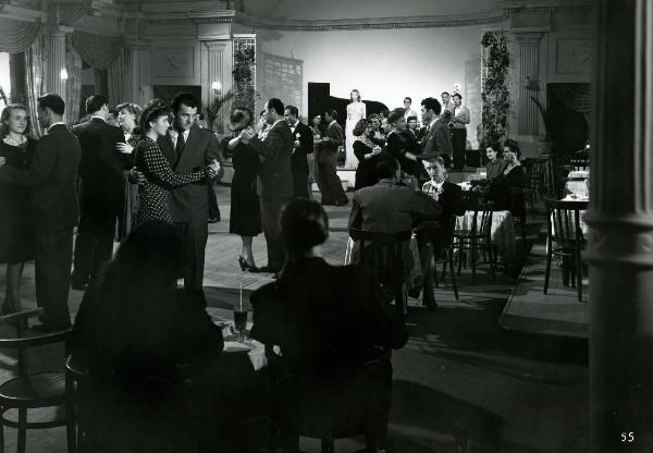 Scena del film "Gioventù perduta" - Germi, Pietro, 1947 - In una sala da ballo, molti attori non identificati danzano e si ristorano stando seduti. A sinistra, Carla Del Poggio, con un vestito a pois, e Massimo Girotti ballano.