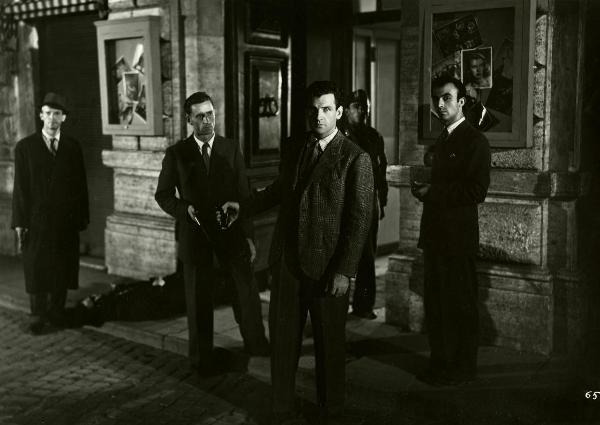 Scena del film "Gioventù perduta" - Germi, Pietro, 1947 - Al centro della scena, Massimo Girotti porge la pistola a un attore non identificato dietro di sé e guarda verso l'obbiettivo. Dietro, quattro attori non identificati.