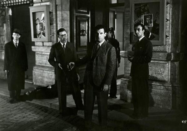Scena del film "Gioventù perduta" - Germi, Pietro, 1947 - Al centro della scena, Massimo Girotti porge la pistola a un attore non identificato dietro di sé e guarda verso l'obbiettivo. Dietro, quattro attori non identificati.