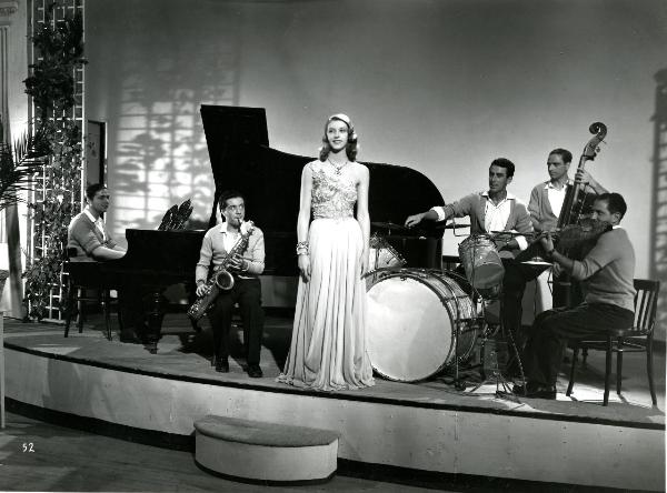 Scena del film "Gioventù perduta" - Germi, Pietro, 1947 - Su un palco, al centro, Leda Vannini mentre guarda verso sinistra. Dietro di lei, alcuni componenti non identificati di una band.