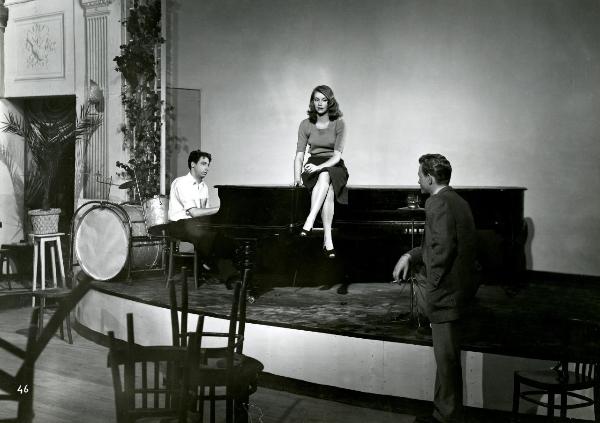 Scena del film "Gioventù perduta" - Germi, Pietro, 1947 - Su un palco, seduta su un pianoforte, Leda Vannini. A destra, Jacques Sernas mentre appoggia una sola gamba sul palcoscenico. A sinistra, un attore non identificato al pianoforte.