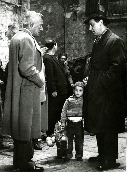 Scena del film "Il giudizio universale" - De Sica, Vittorio, 1961 - A sinistra, Vittorio De Sica con la sigaretta nella mano sinistra. A destra, Alberto Sordi che tiene per mano Carmine Fenari. I due attori si guardano.