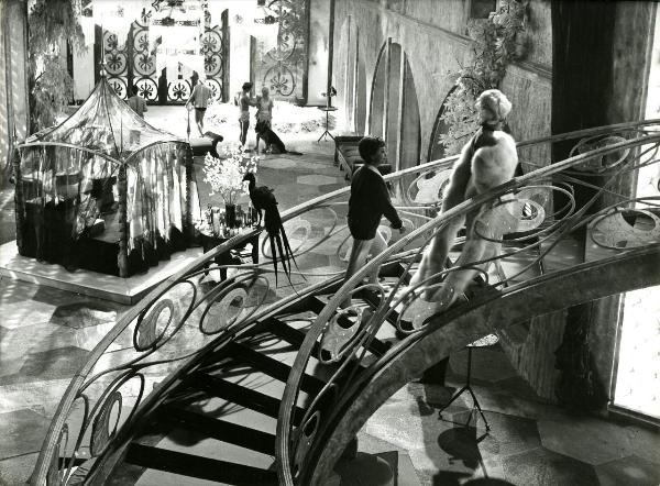 Scena del film "Giulietta degli spiriti" - Fellini, Federico, 1965 - In un grande atrio, due attrici non identificate di profilo salgono le scale. In secondo piano, vicino a un baldacchino, alcuni attori non identificati.