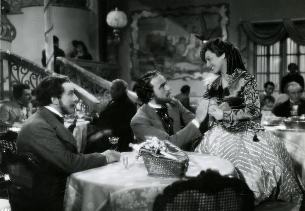 Scena del film "Giuseppe Verdi" - Gallone, Carmine, 1938 - Tre attori non identificati seduti a una tavola imbandita. L'attore al centro, tiene le mani dell'attrice al suo fianco.







