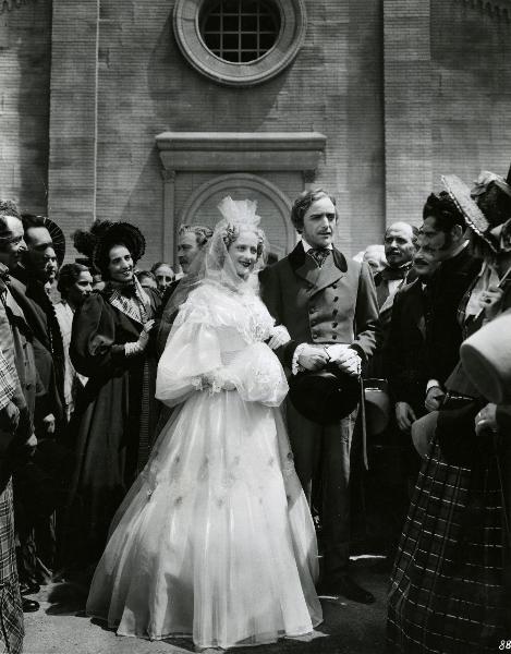 Scena del film "Giuseppe Verdi" - Gallone, Carmine, 1938 - Di fronte a una chiesa, Germana Paolieri e Fosco Giachetti in abiti nunziali. Attorno a loro, alcuni attori non identificati.
