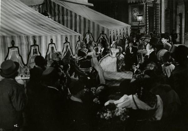 Scena del film "Giuseppe Verdi" - Gallone, Carmine, 1938 - In uno spiazzo con dei tendoni, due attori non identificati al centro della scena recitano. Intorno a loro, una folla di attori non identificati.
