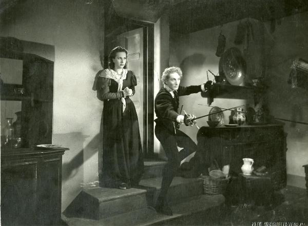 Scena del film "La gondola del Diavolo" - Campogalliani, Carlo, 1946 - Su alcuni gradini, Alfredo Varelli impugna due fioretti in entrambe le mani. Dietro di lui, Loredana.
