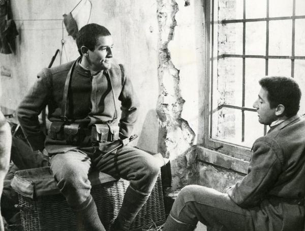 Scena del film "La grande guerra" - Monicelli, Mario, 1959 - Vicino a una finestra a inferriate: a sinistra, Vittorio Gassman seduto con le mani dentro le tasche dei pantaloni, guarda a destra verso Alberto Sordi.

