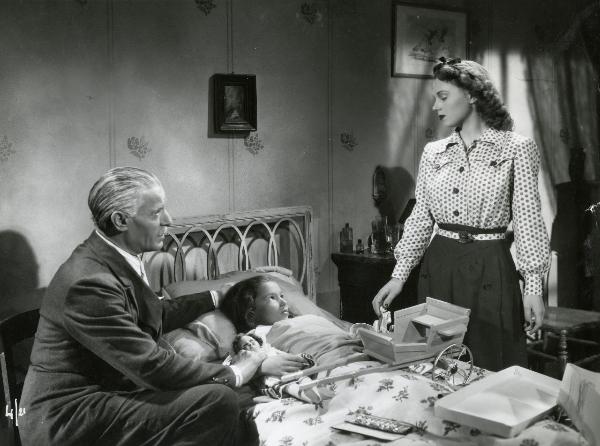 Scena del film "Gran premio" - Musso, Giuseppe, Scarpelli, Umberto, 1957 - Distesa a letto, Mariù Pascoli. Seduto accanto a lei, Luis Hurtado. A destra, in piedi, Luisella Beghi.

