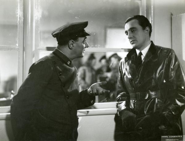 Scena del film "Grandi magazzini" - Camerini, Mario, 1939 - In impermeabile lucido, a destra, Vittorio De Sica. A sinistra, Virgilio Riento gli parla gesticolando con la mano sinistra.





