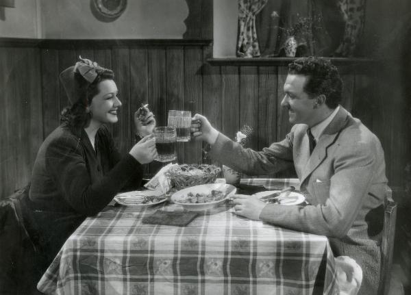 Scena del film "La Granduchessa si diverte" - Gentilomo, Giacomo, 1940 - Seduti a una tavola imbandita, Paola Barbara e Otello Toso, sorridenti, brindano guardandosi negli occhi.
