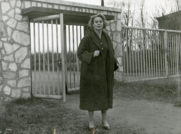 Scena del film "Il grido" - Antonioni, Michelangelo, 1957 - Al di fuori di una cancellata, figura intera di Alida Valli mentre guarda a sinistra.









