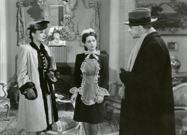 Scena del film "La guardia del corpo" - Bragaglia, Carlo Ludovico, 1942 - In un salotto: Clara Calamai, a sinistra e Sergio Tofano, a destra, si guardano. Tra di loro, un'attrice non identificata nei panni di una cameriera.
