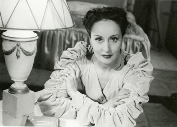 Scena del film "La guardia del corpo" - Bragaglia, Carlo Ludovico, 1942 - Primo piano di Clara Calamai a braccia conserte. Di fianco a lei, una lampada e un libro.

