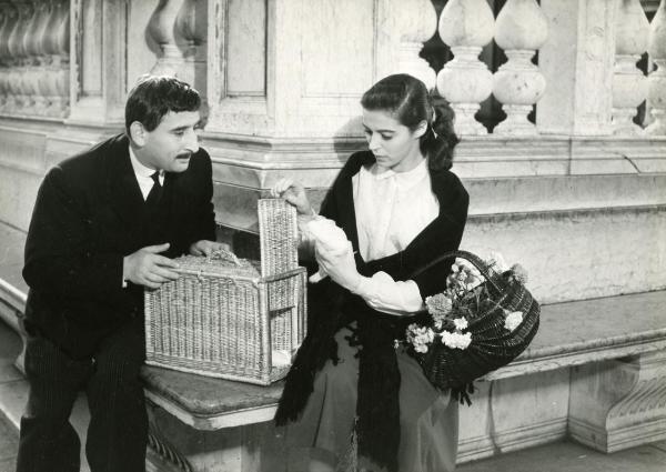 Scena del film "Ho scelto l'amore" - Zampi, Mario, 1952 - Seduti su una panca in marmo: a sinistra, Renato Rascel e a destra, Marisa Pavan. L'attrice sta aprendo una gabbia in vimini.
