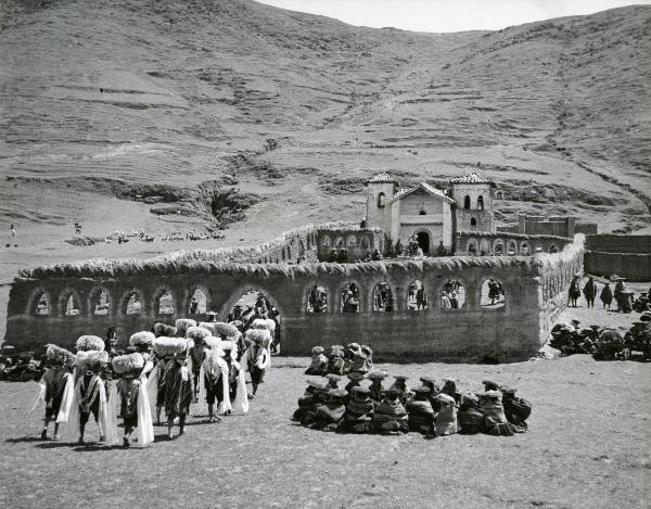 Scena del film "L'impero del sole" - Craveri, Mario, Gras, Enrico, Moser, Giorgio, 1956 - In mezzo ai monti: all'interno del cortile di una chiesa stanno entrando molti attori non identificati in abiti tradizionali.





