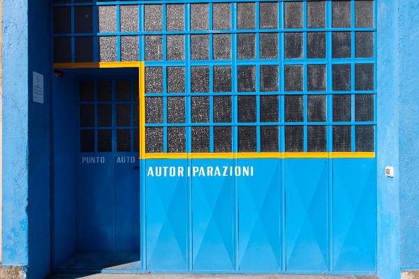 Milano - Particolare dell'ingresso di un'autofficina - Porta in metallo colorato e vetro - Muri - Ombre