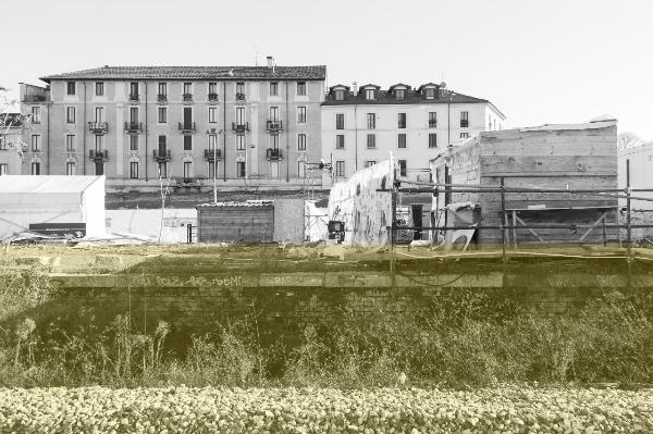 Milano - Scali ferroviari - Scalo Porta Genova - Sassi - Vegetazione - Muro di cinta - Aree, attrezzature e materiali di servizio - Rimesse in legno - Ponteggi - Palazzi, sullo sfondo